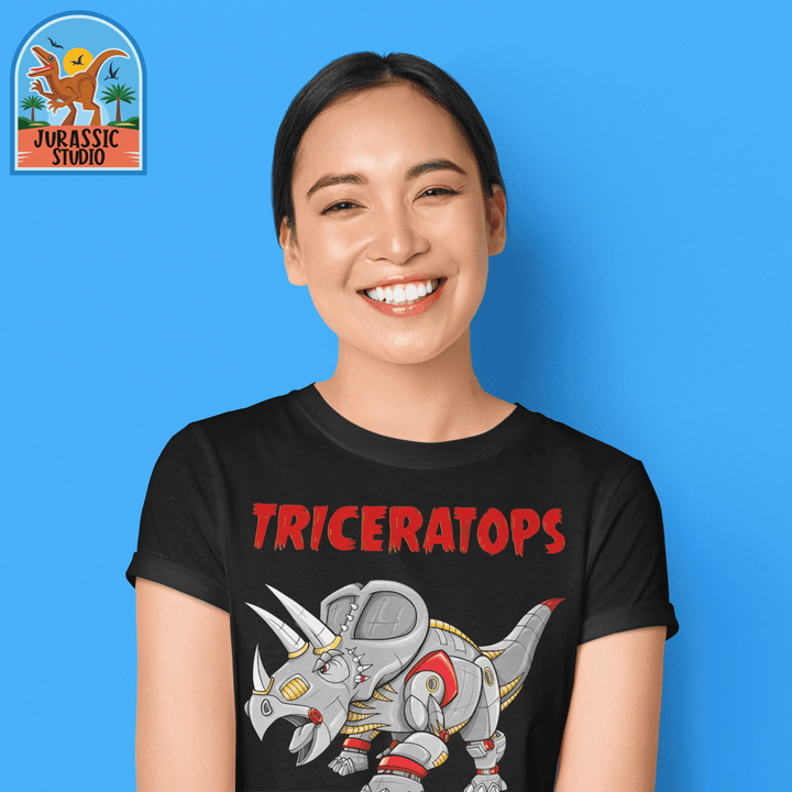 A smiling woman poses before a blue backdrop in the Women Robot Triceratops T-Shirt by Jurassic Studio, featuring a black shirt with a robot triceratops and Triceratops in red. Jurassic Studio logo marks it as an exclusive womens dinosaur tee.