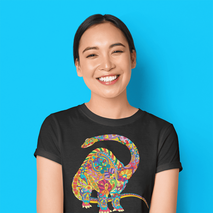 A smiling person stands before a bright blue background, wearing the Jurassic Studio Women Brontosaurus Zentangle T-Shirt featuring a colorful patterned dinosaur graphic.