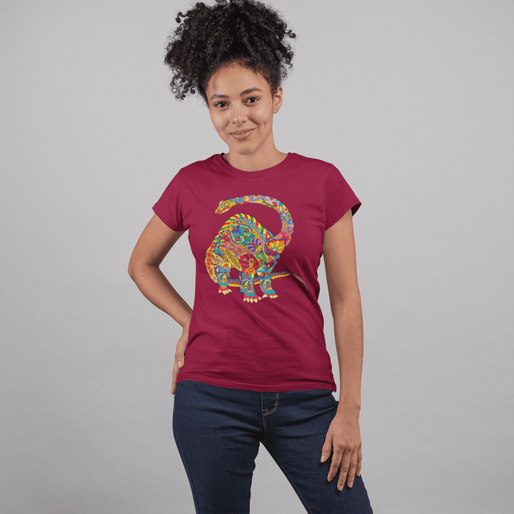 A smiling woman with curly hair stands against a light gray background, wearing a maroon Women Brontosaurus Zentangle T-Shirt by Jurassic Studio, featuring an intricate dinosaur illustration.