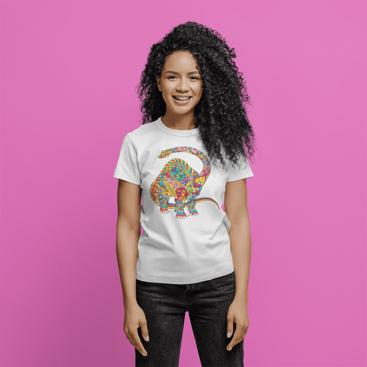 A woman with curly hair smiles against a pink background, wearing the Jurassic Studio Women Brontosaurus Zentangle T-Shirt made of soft Airlume cotton and featuring a colorful patterned dinosaur graphic.