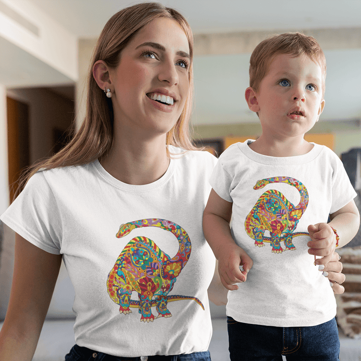 A smiling woman and child wear Jurassic Studio’s Women Brontosaurus Zentangle T-Shirts, each with a colorful floral dinosaur graphic, while standing indoors in a modern living space.
